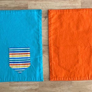 May include: Two placemats, one turquoise blue and one orange, each with a colorful striped pocket sewn on.