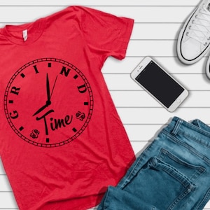 Può includere: Maglietta rossa con un grafico di orologio nero che dice "Grind Time" con simboli di dollaro attorno al quadrante dell'orologio.