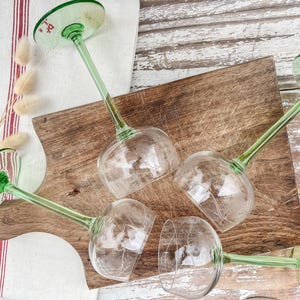 Op de afbeelding: Vier groene gesteelde wijnglazen met heldere glazen kommen. De glazen zijn gerangschikt op een houten snijplank.