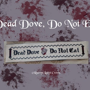 May include: A white cross-stitch sampler with black thread, featuring the text "Dead Dove, Do Not Eat" in a gothic font. The sampler is framed with a black border and a red dove is stitched in the center.