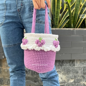 May include: A small purple crocheted bag with white trim and purple flower accents. The bag has a white crocheted handle.
