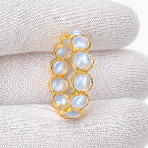 May include: A gold ring featuring a series of oval, iridescent moonstone gemstones. The ring is set in a gold band, with each stone individually set. The ring is displayed on a white background.