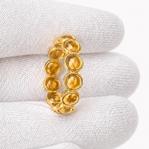 May include: A gold ring featuring a series of round, amber-colored gemstones. The gemstones are set closely together, creating a continuous band of color. The ring is displayed against a white background.