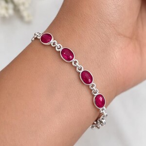 Pode incluir: Uma pulseira de prata com pedras preciosas ovais vermelho escuro. A pulseira é composta por uma série de segmentos ligados, cada um com uma pedra preciosa. As pedras preciosas são engastadas em metal prateado. A pulseira é usada no pulso.