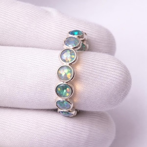 May include: A silver ring featuring a series of oval-cut opals. The opals display a range of colors, including green, blue, and hints of yellow. The ring is set in a simple, elegant band.