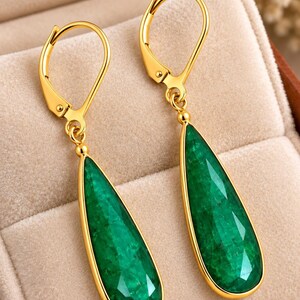 Peut inclure: Une paire de boucles d'oreilles à fermoir levier en or avec des pierres vertes facettées en forme de goutte. Les boucles d'oreilles présentent une monture en métal doré poli qui encadre les pierres précieuses vertes texturées.