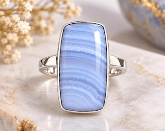 May include: A silver ring featuring a large, rectangular, light blue lace agate gemstone with distinct white horizontal banding. The stone is set in a smooth, polished silver bezel with a simple, slender silver band.