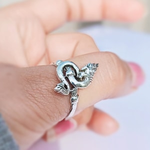 Puede incluir: Un anillo de plata con un diseño detallado de un dragón o serpiente. El anillo se lleva en un dedo.