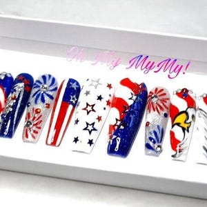 May include: Set of ten long, artificial fingernails with a patriotic theme. The nails are decorated with red, white, and blue stripes, stars, fireworks, and an eagle. The text "Oh My My!" is visible in the background.
