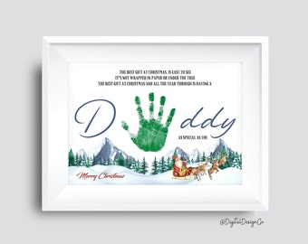 May include: A framed Christmas print with a green handprint, the word "Daddy", and the text "Merry Christmas". The print includes a winter scene with mountains, trees, and Santa's sleigh.