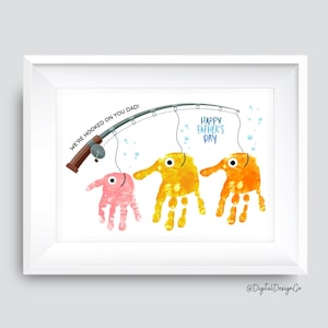 May include: Framed art print with a fishing theme. The artwork features handprint fish in shades of pink, yellow, and orange, suspended from a fishing rod. Text reads "We're hooked on you Dad!" and "Happy Father's Day."