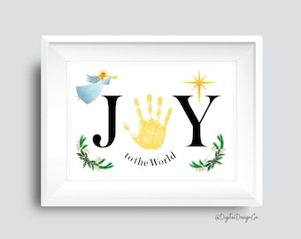 May include: White framed print with the word "JOY" in black letters, a yellow handprint in place of the "O", and the words "to the World" below. An angel, star, and sprigs of greenery complete the design.