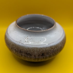 May include: A small, white ceramic bowl with a brown glaze around the rim. The bowl has a rounded shape and a smooth, glossy finish.