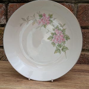 May include: A white ceramic bowl with a silver rim and a floral design featuring pink flowers and green leaves.