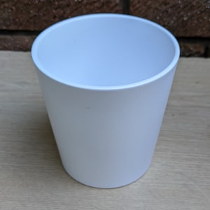 Puede incluir: Una maceta cilíndrica blanca de plástico. La maceta está vacía y tiene una superficie lisa.