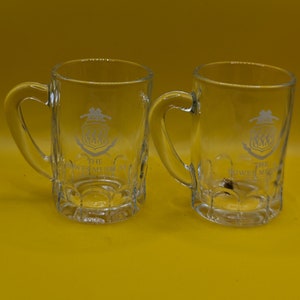 May include: Two clear glass mugs with handles. Each mug features a white logo that reads "The Bowes Museum" with a crest design.