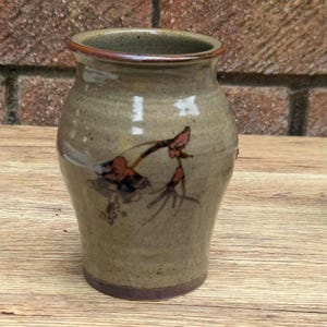 May include: A handcrafted ceramic vase with a speckled, earthy tone. The vase features a flared rim and a painted floral design in shades of brown and red. The vase is approximately 6 inches tall.