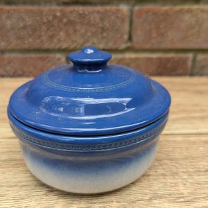 May include: A blue and white ceramic jar with a lid. The jar has a white base and a blue top with a decorative border. The lid is also blue with a white border.