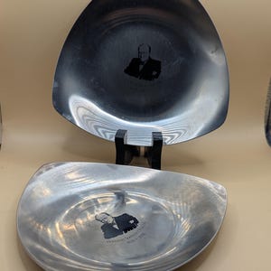 Puede incluir: Dos platos de servir triangulares de plata con una imagen en blanco y negro de un hombre y el texto "Winston Spencer Churchill 1874 - 1965" en el plato inferior.