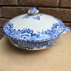 May include: A white ceramic serving bowl with a blue and white floral pattern. The bowl has a lid with a knob on top.