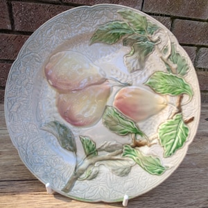 May include: A white ceramic plate with a raised design of pears and leaves. The pears are pink and yellow and the leaves are green.