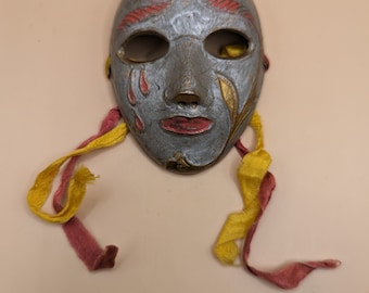 May include: A silver and gold masquerade mask with red and gold painted details. The mask has a teardrop design on each side and is attached to two ribbons, one red and one yellow.