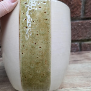 Può includere: Un vaso di ceramica bianco con una fascia verticale di smalto verde e marrone. Lo smalto ha un motivo maculato.