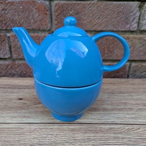 Könnte beinhalten: Eine blaue Teekanne aus Keramik mit einer passenden Tasse. Die Teekanne hat einen Deckel und einen Griff. Die Tasse ist auf die Teekanne gestapelt.