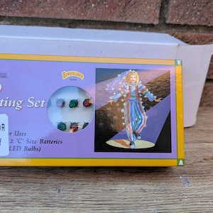 Könnte beinhalten: Eine Schachtel mit 20 LED-Lichtern für den Innenbereich. Die Schachtel ist gelb und lila mit dem Text "LED Lighting Set". Die Schachtel hat eine Illustration einer Person in einem bunten Outfit und ein Bild der LED-Leuchten.