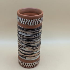 Könnte beinhalten: Eine Terrakotta-Vase mit einem braunen, weißen und schwarzen Streifenmuster. Die Vase hat oben und unten einen weißen Dekorband.