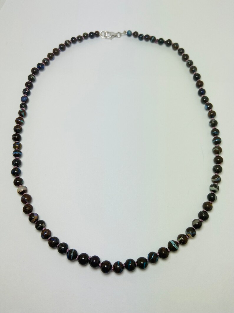 May include: A necklace made of dark brown, blue, and white patterned beads with a silver clasp.