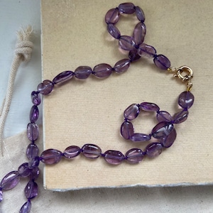 Op de afbeelding: Een ketting van paarse amethist edelstenen met een gouden sluiting. De ketting ligt op een stuk papier met de tekst "Moed, lieve hart."