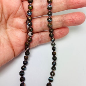 May include: A necklace made of dark brown, black, and blue opal beads with a purple thread running through the center of the beads.