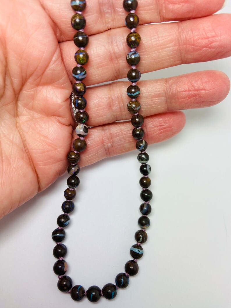 May include: A necklace made of dark brown, black, and blue opal beads with a purple thread running through the center of the beads.