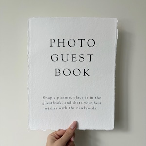May include: White sign with black text that reads "PHOTO GUEST BOOK" and "Snap a picture, place it in the guestbook, and share your best wishes with the newlyweds."