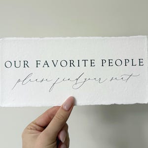 May include: White sign with the text "OUR FAVORITE PEOPLE please find your seat" in black lettering.