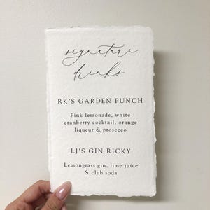 May include: A white card with the text "signature drinks" written in cursive. Below the text are two drink recipes: "RK'S GARDEN PUNCH" and "LJ'S GIN RICKY".