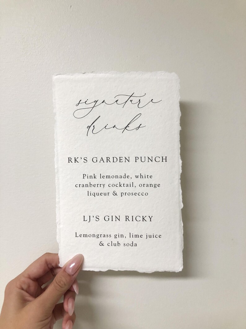 May include: A white card with the text "signature drinks" written in cursive. Below the text are two drink recipes: "RK'S GARDEN PUNCH" and "LJ'S GIN RICKY".