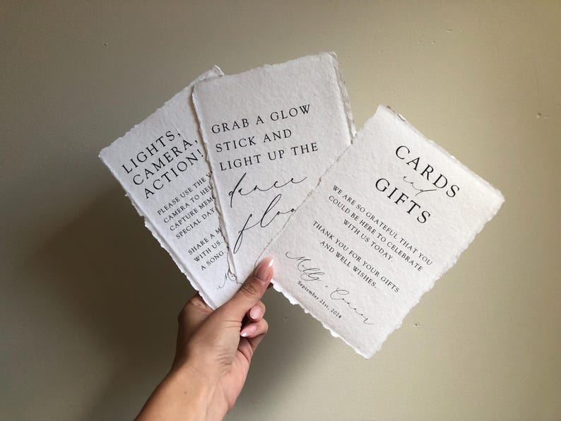 May include: Three white cards with black text. The first card says "Lights, Camera, Action!" and has instructions to use the camera to capture memories. The second card says "Grab a glow stick and light up the dance floor". The third card says "Cards and Gifts" and expresses gratitude for the guests' presence and gifts. The cards are decorated with a rustic, hand-torn edge.