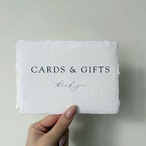 May include: A white card with the text "CARDS & GIFTS" in black lettering and "thank you" in cursive handwriting.