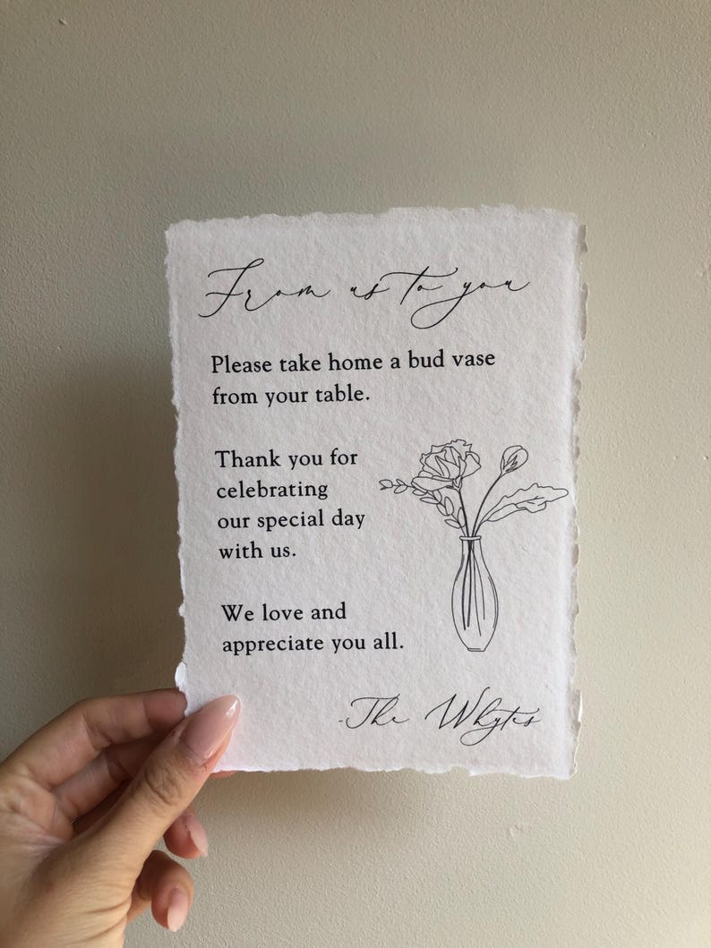 May include: A white card with black text that reads "From us to you. Please take home a bud vase from your table. Thank you for celebrating our special day with us. We love and appreciate you all. - The Wrights." A simple line drawing of a vase with flowers is in the upper right corner.
