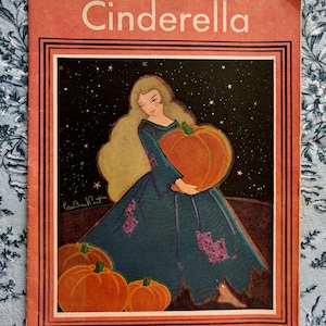 May include: Vintage "Cinderella" book cover. The cover shows a woman in a teal dress holding a large orange pumpkin, with smaller pumpkins at her feet. The background is a starry night sky, with the title "Cinderella" at the top.