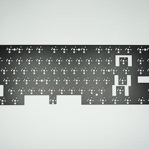 May include: A black metal keyboard plate with cutouts for key switches. The plate has a rectangular shape and is designed for a standard keyboard layout.