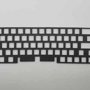 Könnte beinhalten: Schwarze Kunststoff-Tastaturplatte mit Ausschnitten für Tastenkontakte. Die Platte ist rechteckig und für ein 60%iges Tastaturlayout ausgelegt.