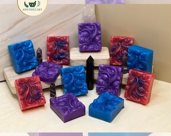 May include: A collection of vibrantly colored, rectangular soaps with intricate swirl designs. The soaps are in shades of blue, red, and purple. The Recovery Witch Apothecary logo is visible in the upper left corner.