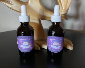 May include: Two dark amber glass bottles with white droppers. Each bottle has a label with the text "The Sandman's Blend" and an illustration of a cartoon character. The bottles are on a black surface.
