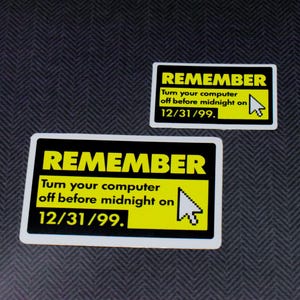 May include: Two rectangular stickers with black borders and yellow text. The top sticker reads "REMEMBER" above the text "Turn your computer off before midnight on 12/31/99." A computer cursor graphic is on the right. The bottom sticker has the same text and graphic.