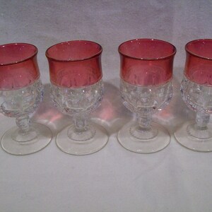 May include: Set of four clear glass stemmed drinking glasses with a red, cranberry colored top. The glasses have a textured, diamond pattern.