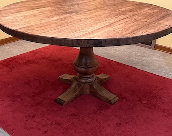 May include: A round wooden dining table with a dark brown base and four legs. The table top is made of light wood with a natural finish. The table is sitting on a red rug.