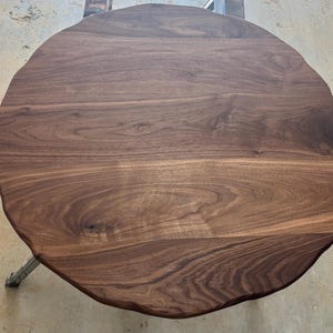 May include: A round, solid wood table with a natural edge. The tabletop is a rich, dark brown with visible wood grain patterns. The table is supported by metal legs.